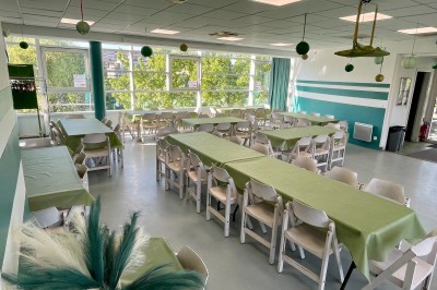 Salle de réunion lumineuse avec des rangées de chaises, des tables et un écran de projection devant des fenêtres donnant sur…