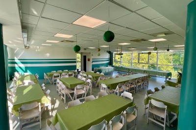 Salle de réunion lumineuse avec des rangées de chaises, des tables et un écran de projection devant des fenêtres donnant sur…