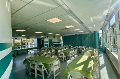 Salle de réunion lumineuse avec des rangées de chaises, des tables et un écran de projection devant des fenêtres donnant sur…