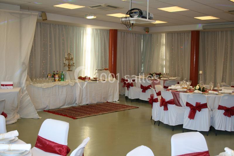 Salle décorée pour un événement avec des tables dressées, des chaises ornées de nœuds rouges et un buffet en arrière-plan.
