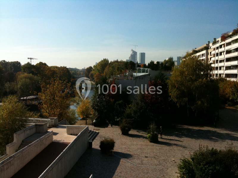 Vue d'un parc urbain avec des arbres aux couleurs automnales, un cours d'eau et des immeubles en arrière-plan.