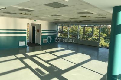 Salle vide avec sol clair, murs verts et blancs, grandes fenêtres, éclairage au plafond et mobilier minimal.