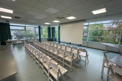Salle vide avec sol clair, murs verts et blancs, grandes fenêtres, éclairage au plafond et mobilier minimal.