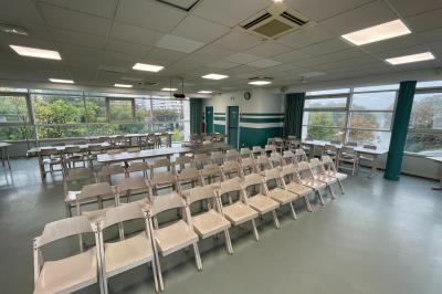 Salle vide avec sol clair, murs verts et blancs, grandes fenêtres, éclairage au plafond et mobilier minimal.