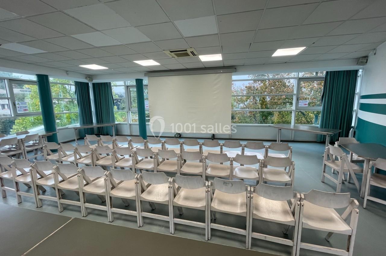 Salle de conférence lumineuse avec des rangées de chaises blanches face à un écran de projection.