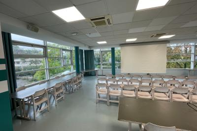 Salle vide avec sol clair, murs verts et blancs, grandes fenêtres, éclairage au plafond et mobilier minimal.