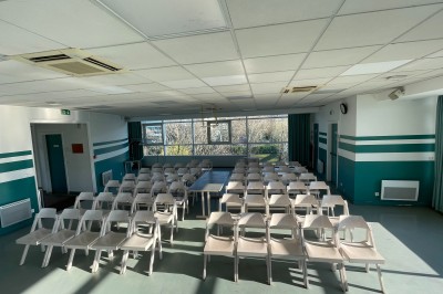 Salle vide avec sol clair, murs verts et blancs, grandes fenêtres, éclairage au plafond et mobilier minimal.