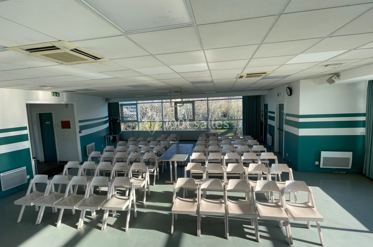 Salle de réunion lumineuse avec des rangées de chaises blanches alignées devant une table centrale.