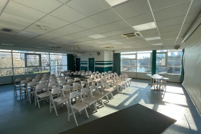 Salle vide avec sol clair, murs verts et blancs, grandes fenêtres, éclairage au plafond et mobilier minimal.