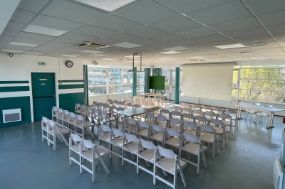 Salle vide avec sol clair, murs verts et blancs, grandes fenêtres, éclairage au plafond et mobilier minimal.
