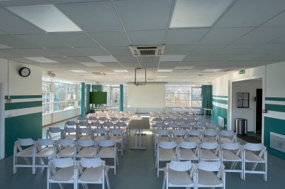 Salle vide avec sol clair, murs verts et blancs, grandes fenêtres, éclairage au plafond et mobilier minimal.