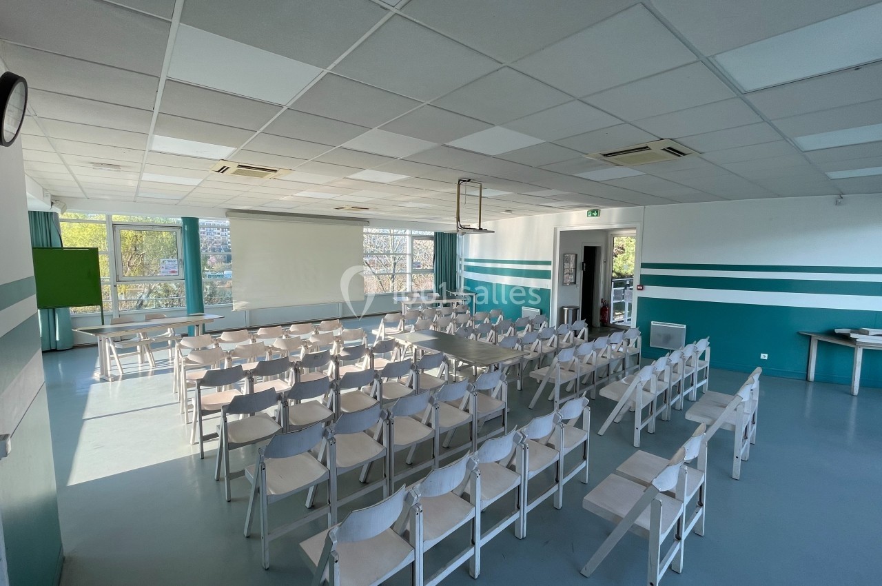 Salle de conférence lumineuse avec des rangées de chaises blanches, un écran de projection et des fenêtres donnant sur l…