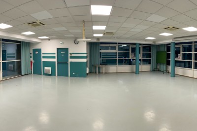 Salle vide avec sol clair, murs verts et blancs, grandes fenêtres, éclairage au plafond et mobilier minimal.