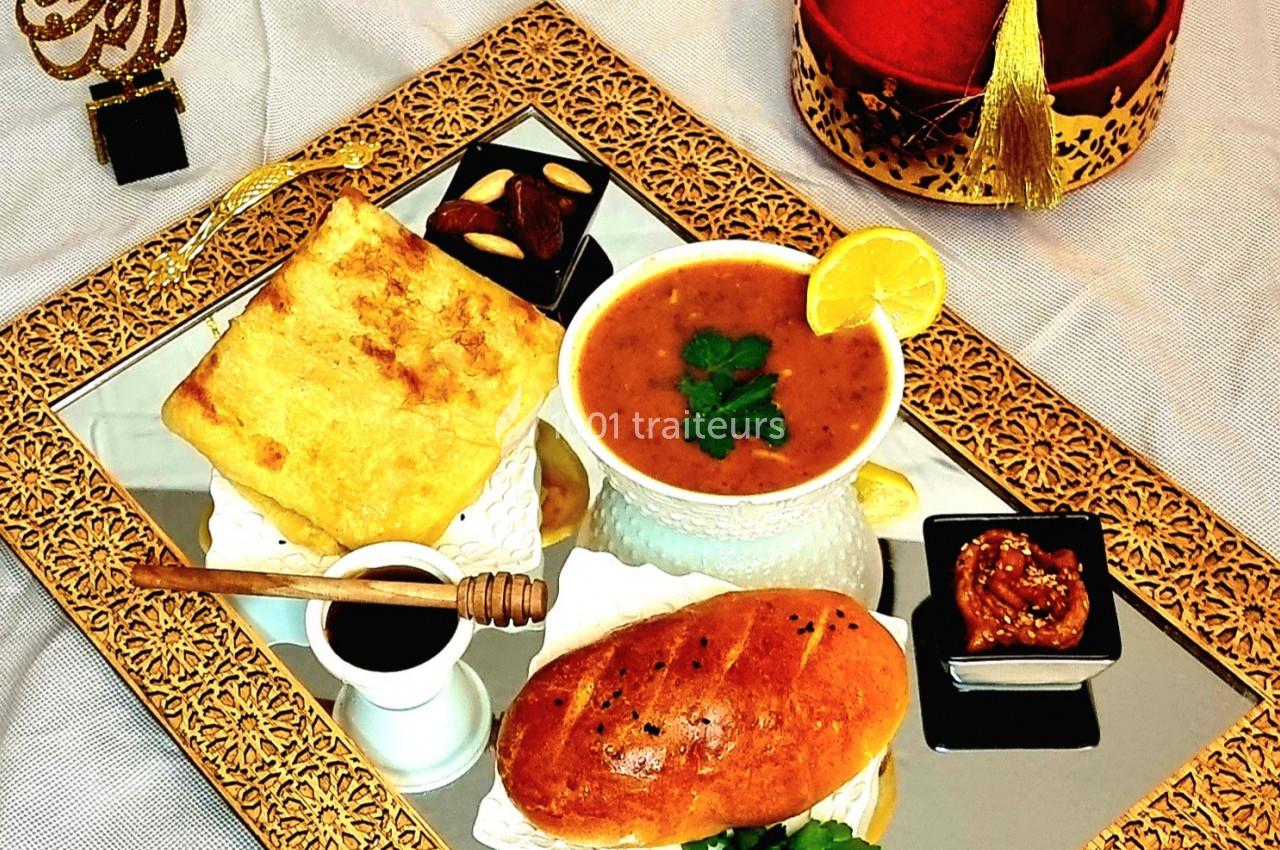 Plateau doré avec soupe, pain, miel, fromage, confiture et chapeau rouge décoratif en arrière-plan.