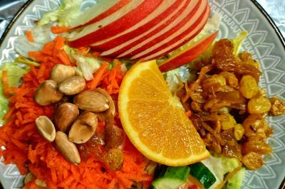 Assiette composée de salade, carottes râpées, amandes, pommes en tranches, raisins secs et une rondelle d'orange.