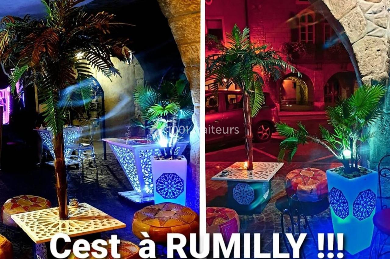 Deux espaces extérieurs décorés avec des palmiers artificiels, éclairages colorés et mobilier de style oriental.