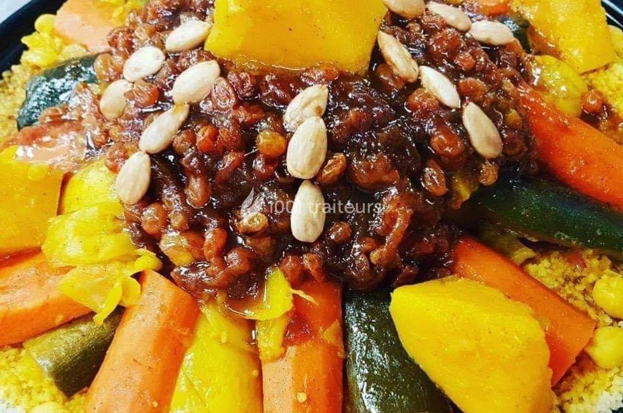 Plat de couscous garni de légumes colorés, raisins secs, amandes et morceaux de courge au centre.