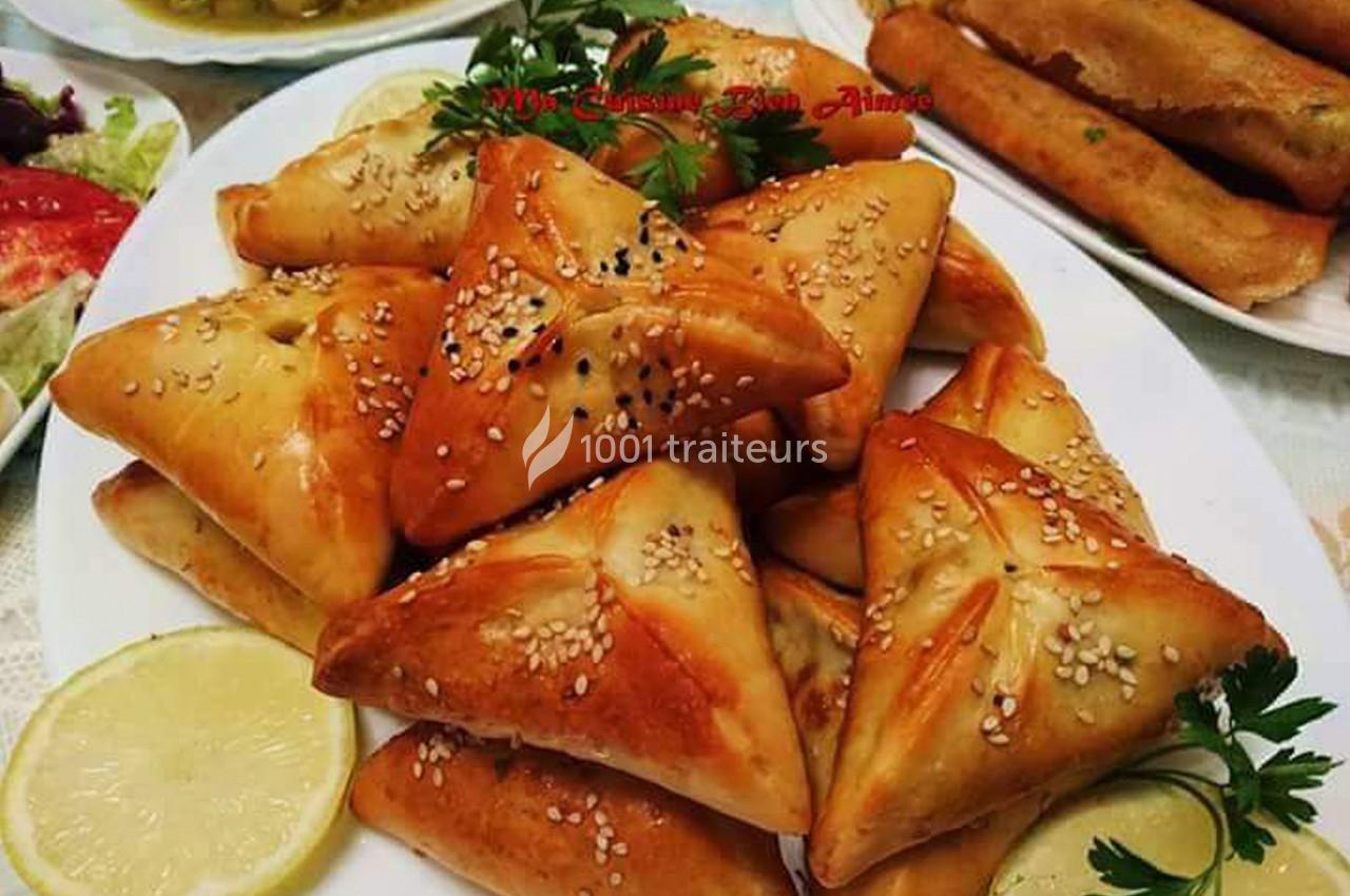 Assortiment de triangles feuilletés dorés garnis, décorés de graines de sésame, servis avec des tranches de citron.