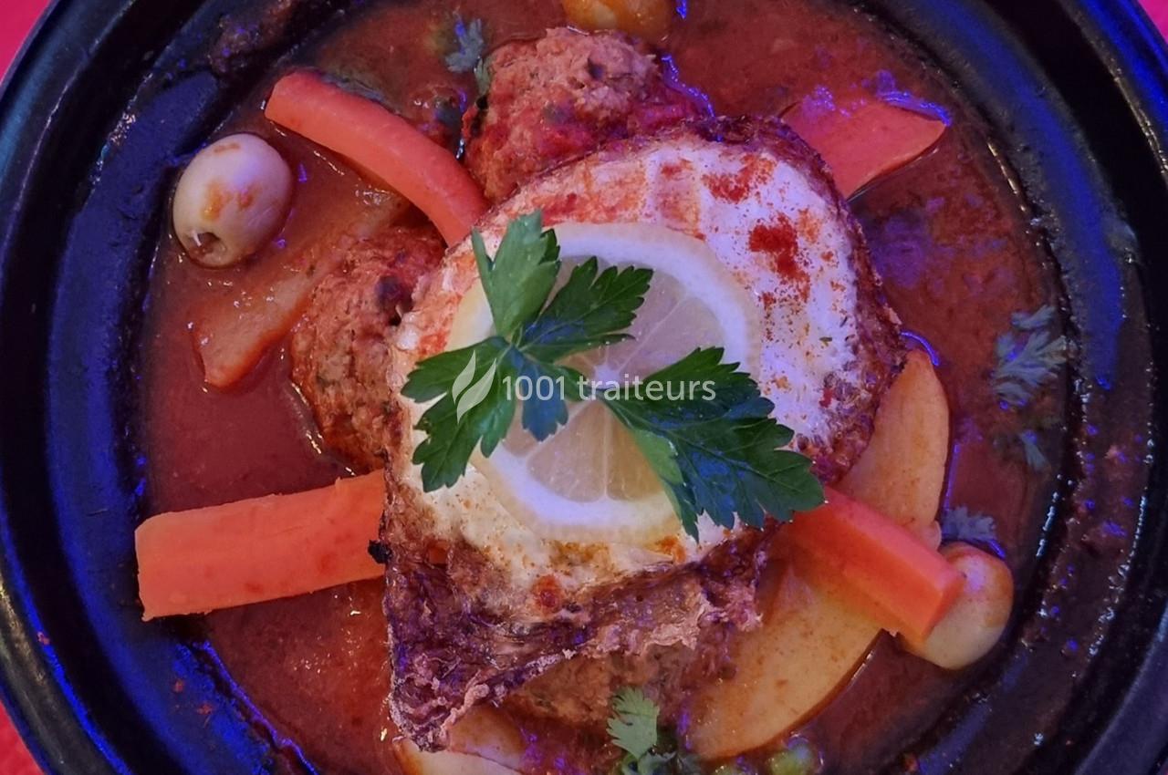 Plat de tajine avec boulettes de viande, œuf, légumes, olives et citron, garni de persil dans une sauce épicée.