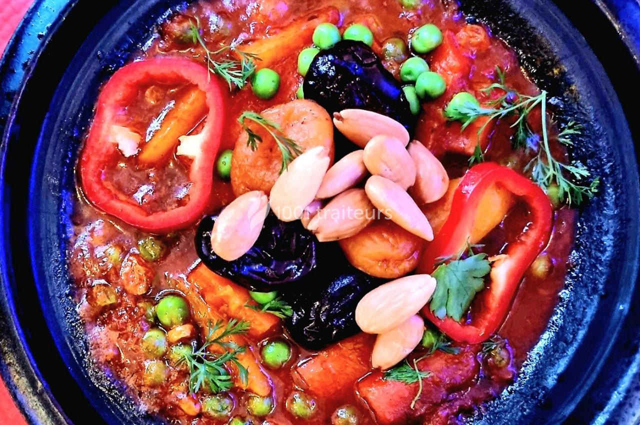 Plat de tajine coloré avec légumes, pois, amandes, pruneaux, rondelles de poivron rouge et herbes fraîches.