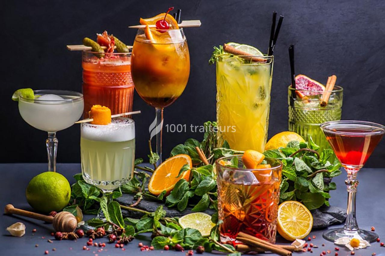 Assortiment de cocktails colorés garnis de fruits et herbes, disposés sur une table avec des agrumes et épices.