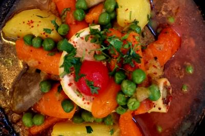 Assiette garnie de légumes variés, morceaux de viande et sauce rouge au centre, présentée sur un lit de salade.