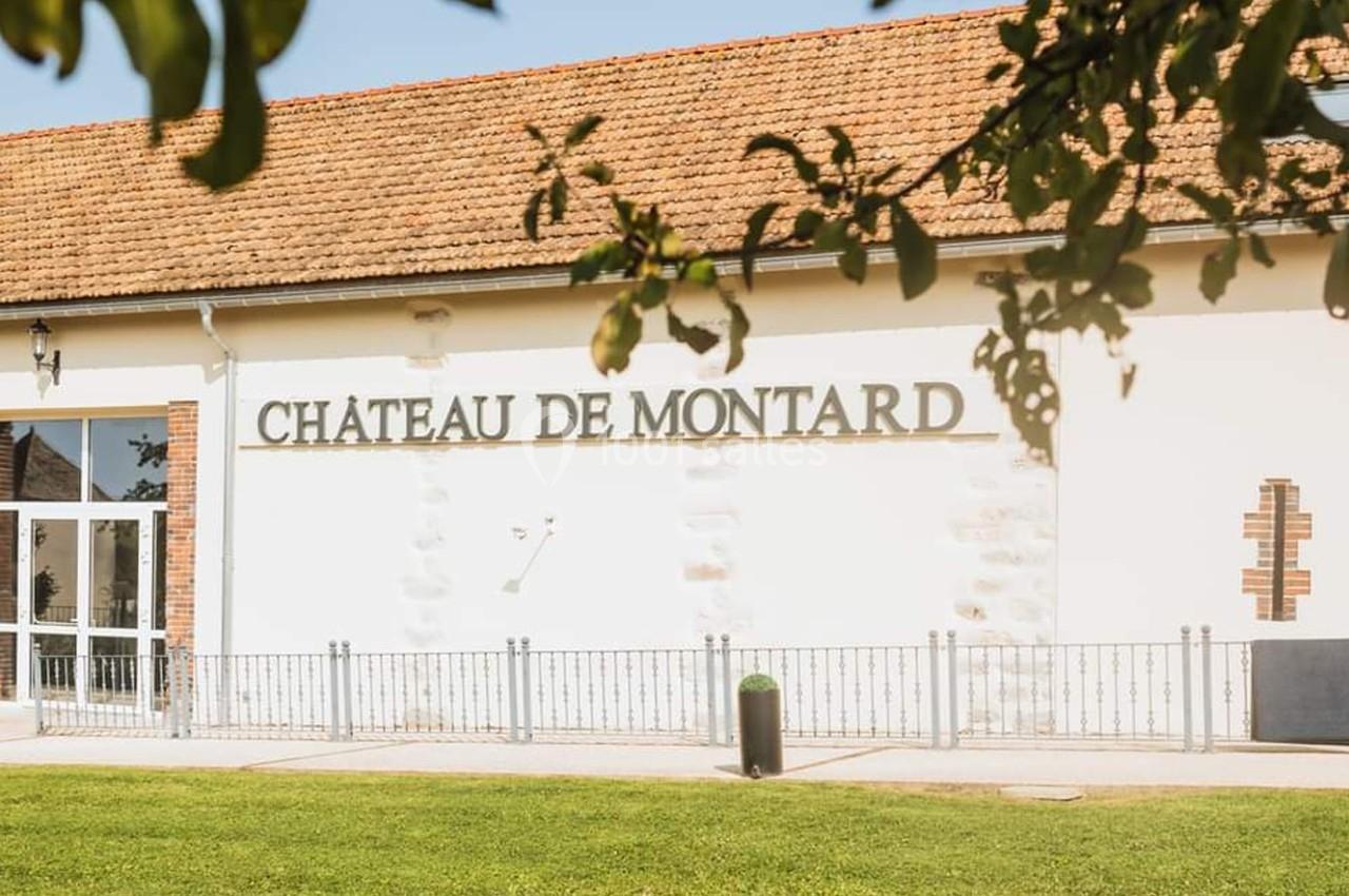 Façade d'un bâtiment avec l'inscription ’Château de Montard’, entourée de pelouse et partiellement ombragée.