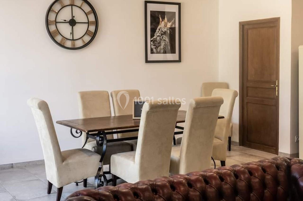 Salle à manger avec table en bois, six chaises beige, horloge murale et cadre décoratif au mur.
