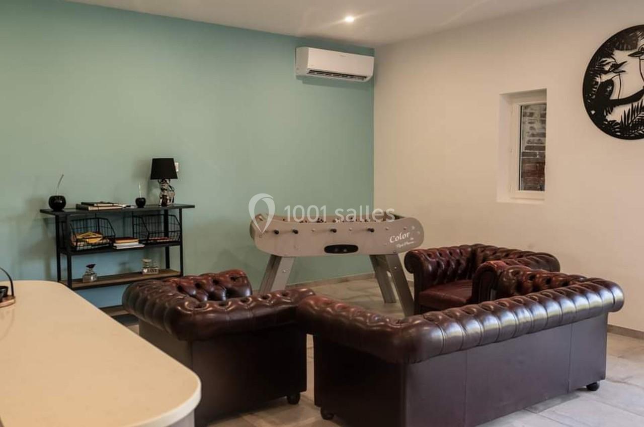 Salle avec murs clairs, baby-foot, canapés en cuir, étagère décorative et climatiseur mural.