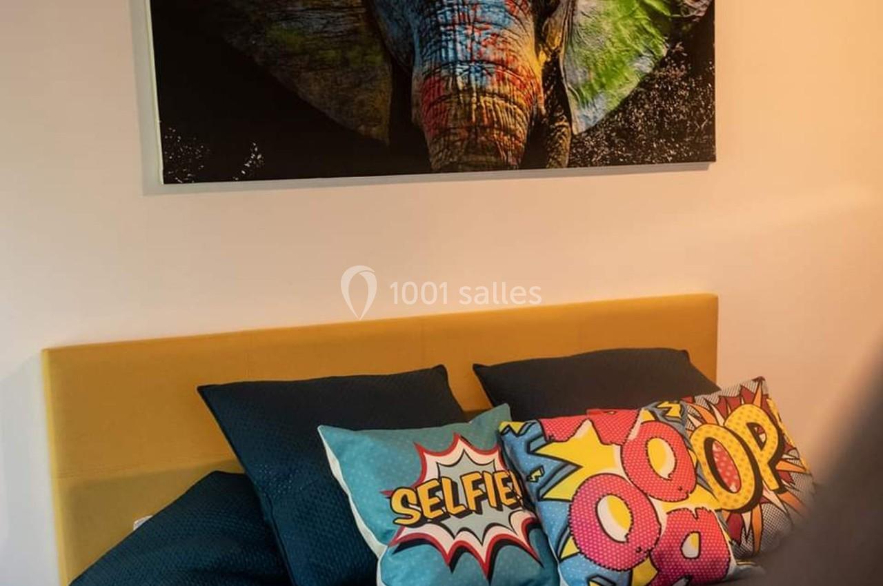 Tableau d'un éléphant coloré accroché au-dessus d'un lit avec une tête de lit jaune et des coussins aux motifs pop art.