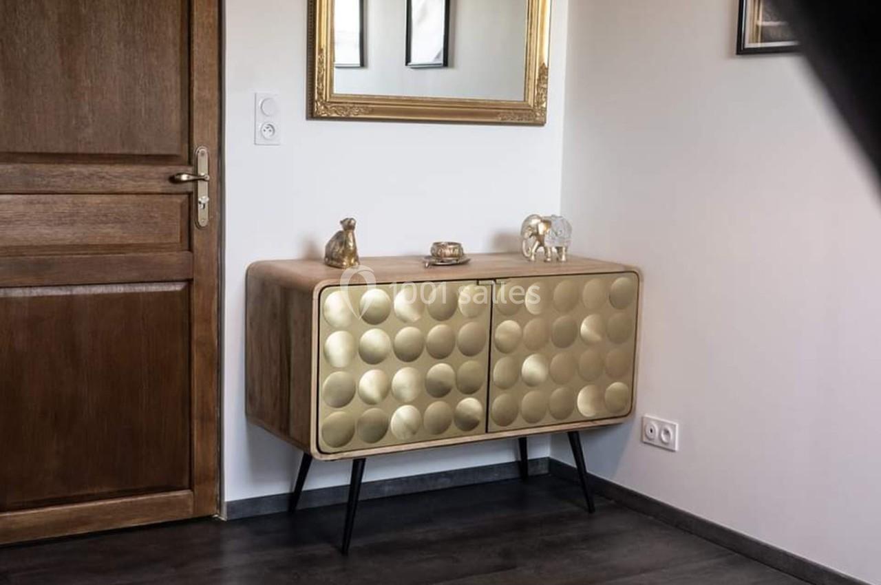 Buffet en bois avec portes dorées texturées, décoré de petites sculptures, placé près d'un miroir et d'une porte en bois.