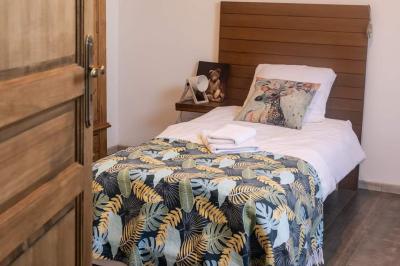 Lit simple avec une tête de lit en bois, couvert d'une couverture à motifs tropicaux, dans une chambre lumineuse.