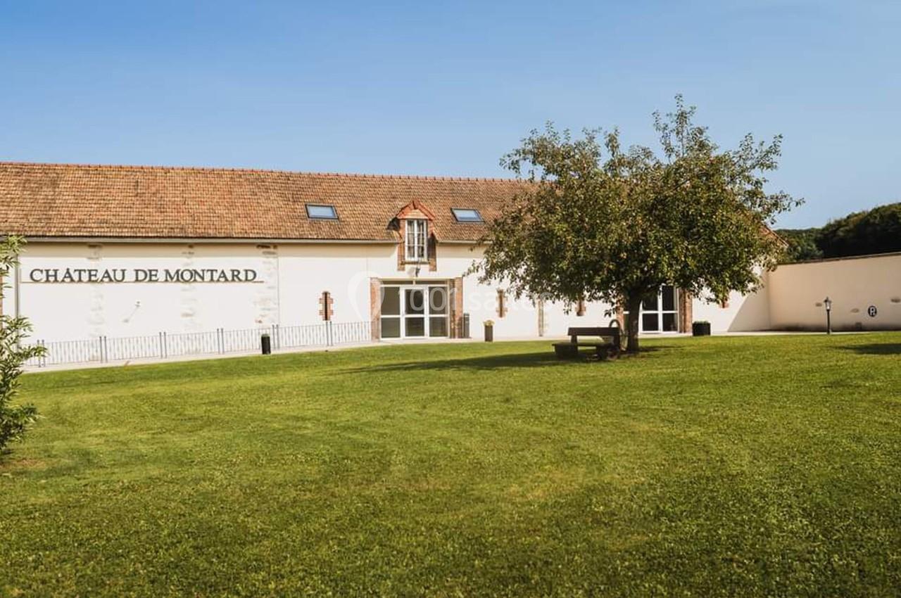 Bâtiment blanc avec toit en tuiles, inscription ’Château de Montard’, pelouse et arbre au premier plan.