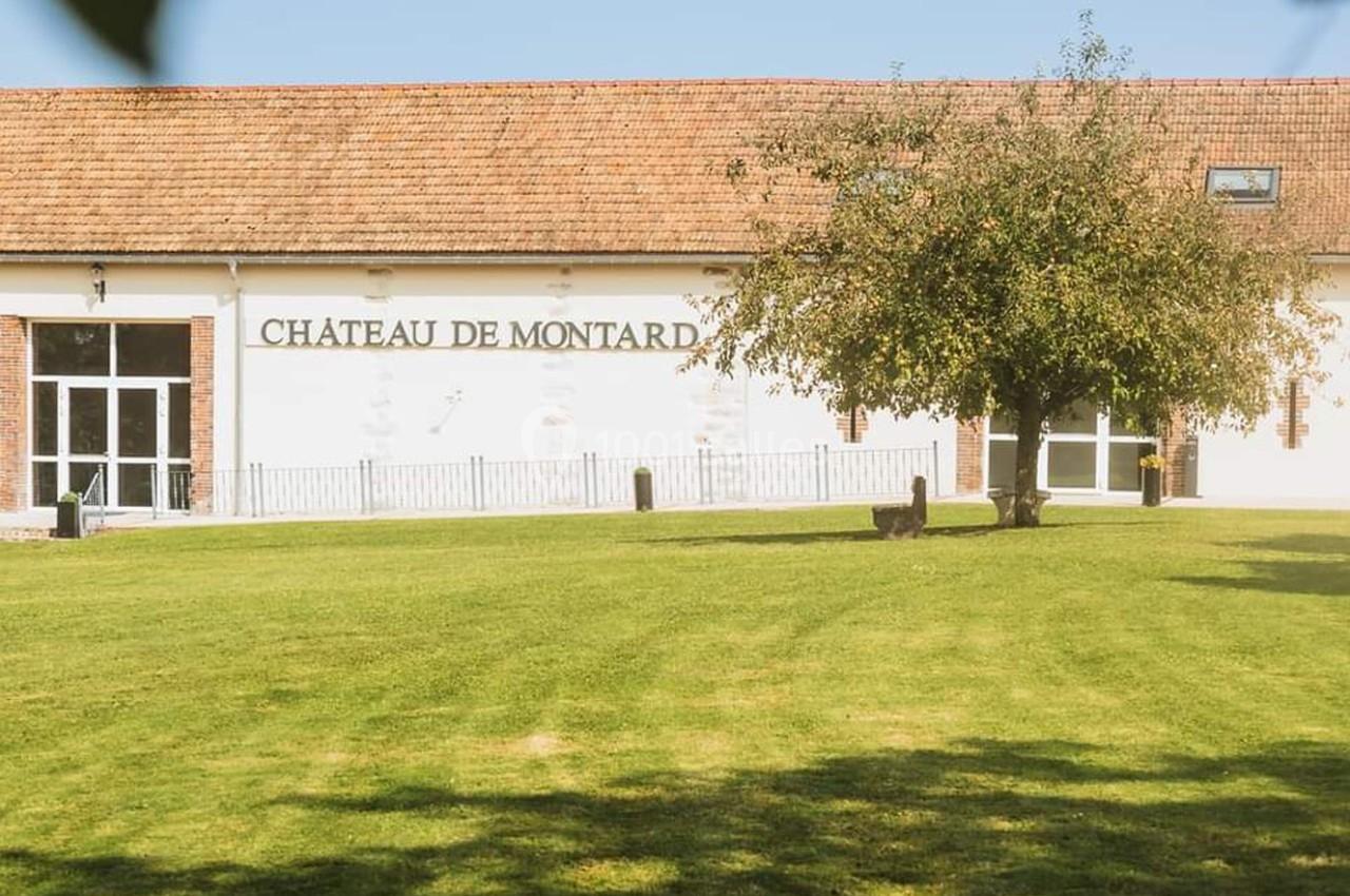 Bâtiment blanc avec toit en tuiles rouges, marqué ’Château de Montard’, entouré d'une pelouse et d'un arbre.