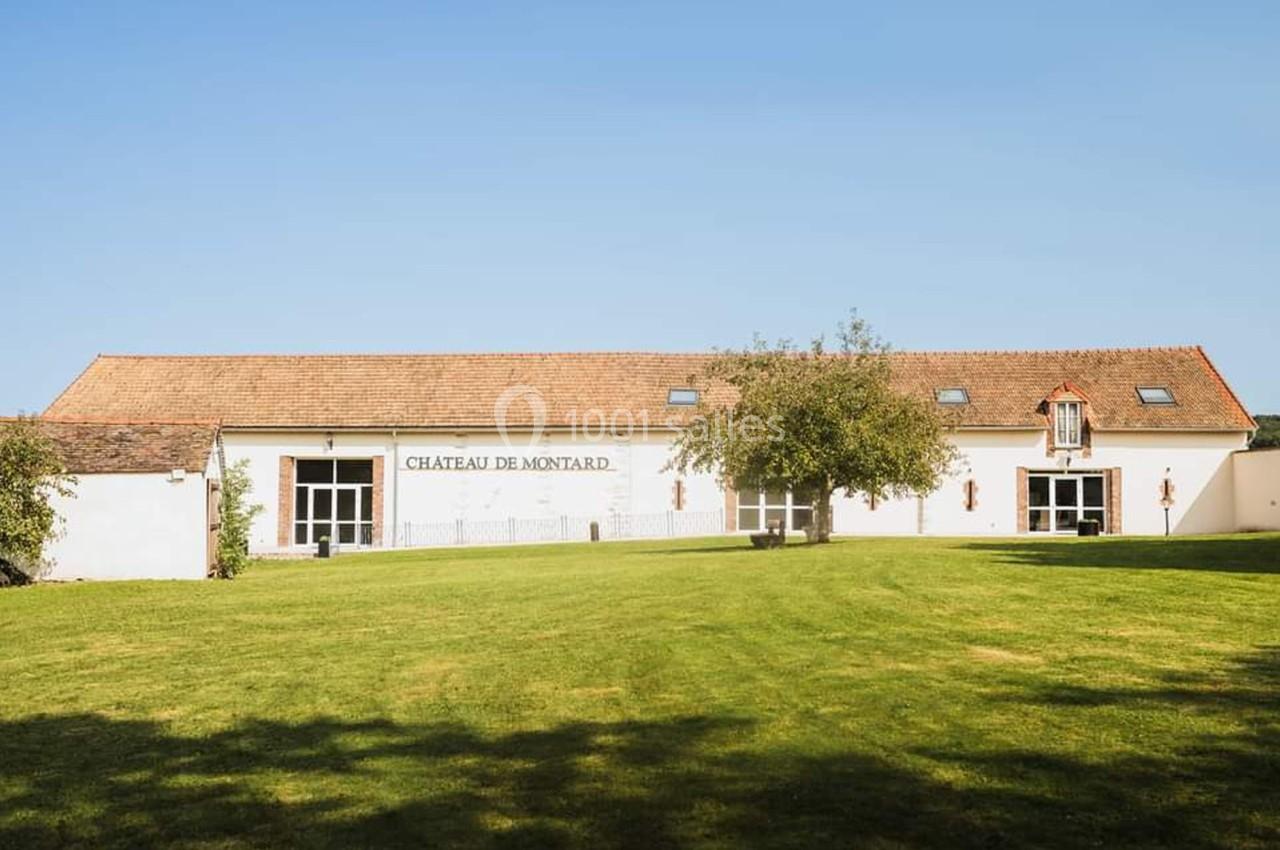 Bâtiment blanc avec toit en tuiles rouges, entouré d'une pelouse et d'arbres sous un ciel dégagé.