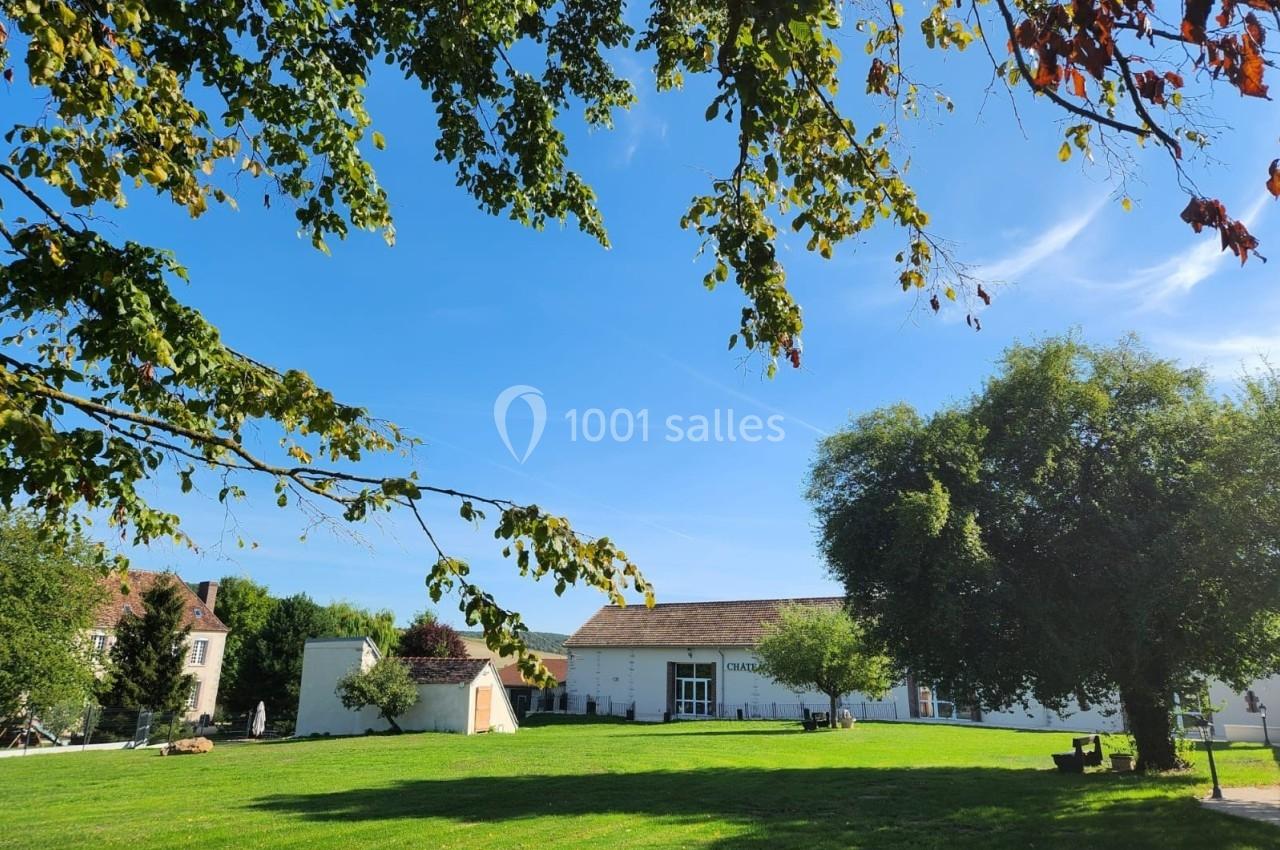 Pelouse verdoyante avec des arbres et un bâtiment clair sous un ciel bleu dégagé.