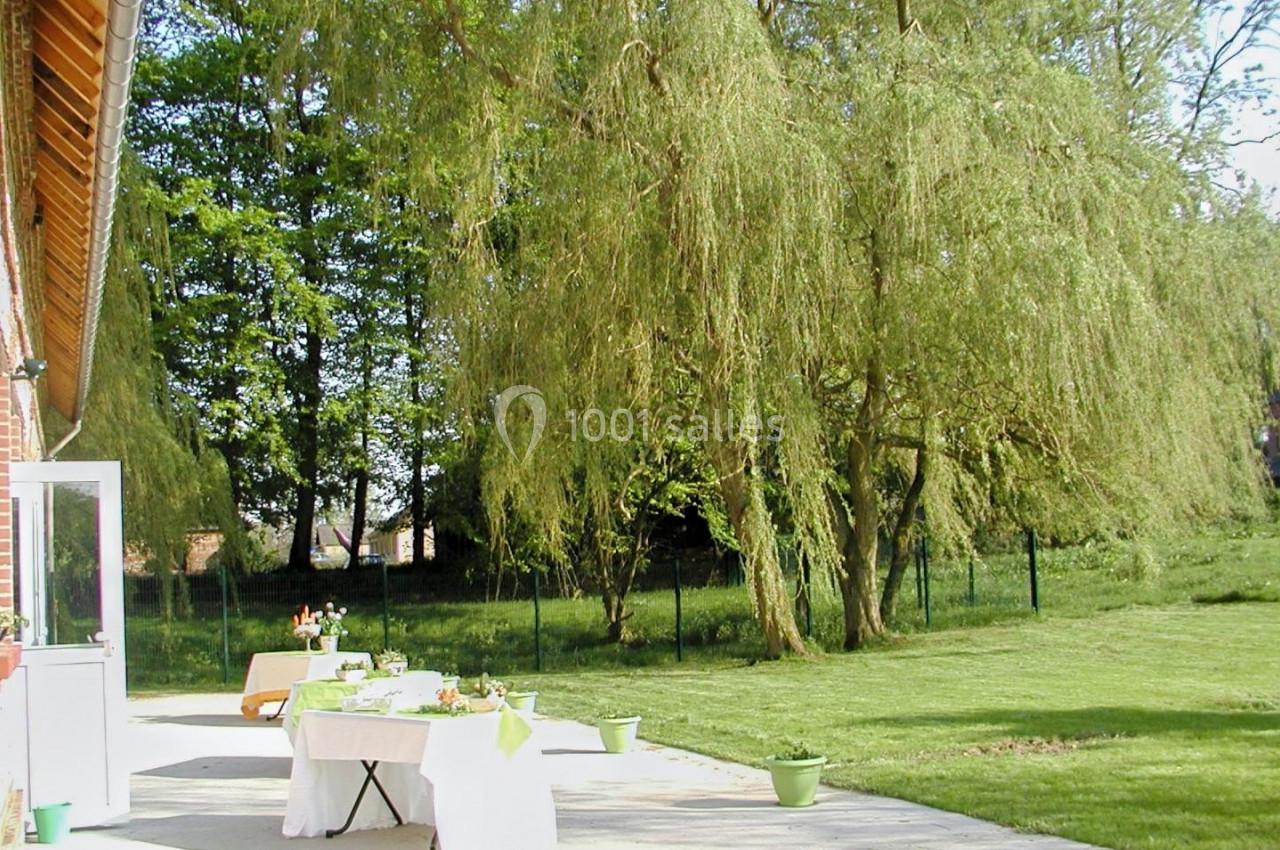 Table dressée en extérieur sur une terrasse, entourée d'arbres et d'une pelouse verdoyante.