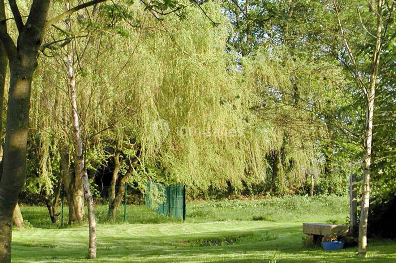 Un jardin verdoyant avec des arbres, une pelouse tondue, un banc en pierre et une clôture en arrière-plan.