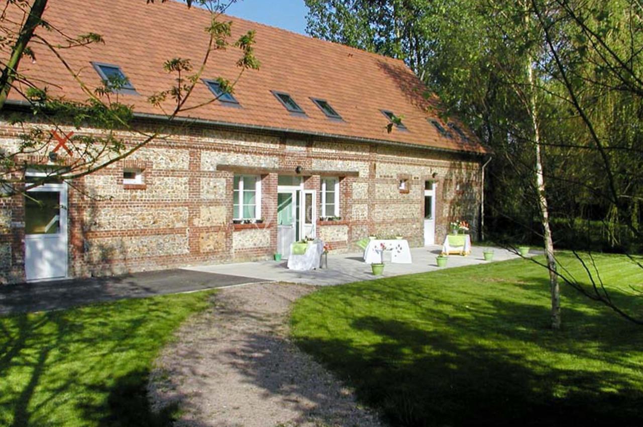 Bâtiment en briques avec toit en tuiles, entouré d'un jardin verdoyant et d'une allée en gravier.