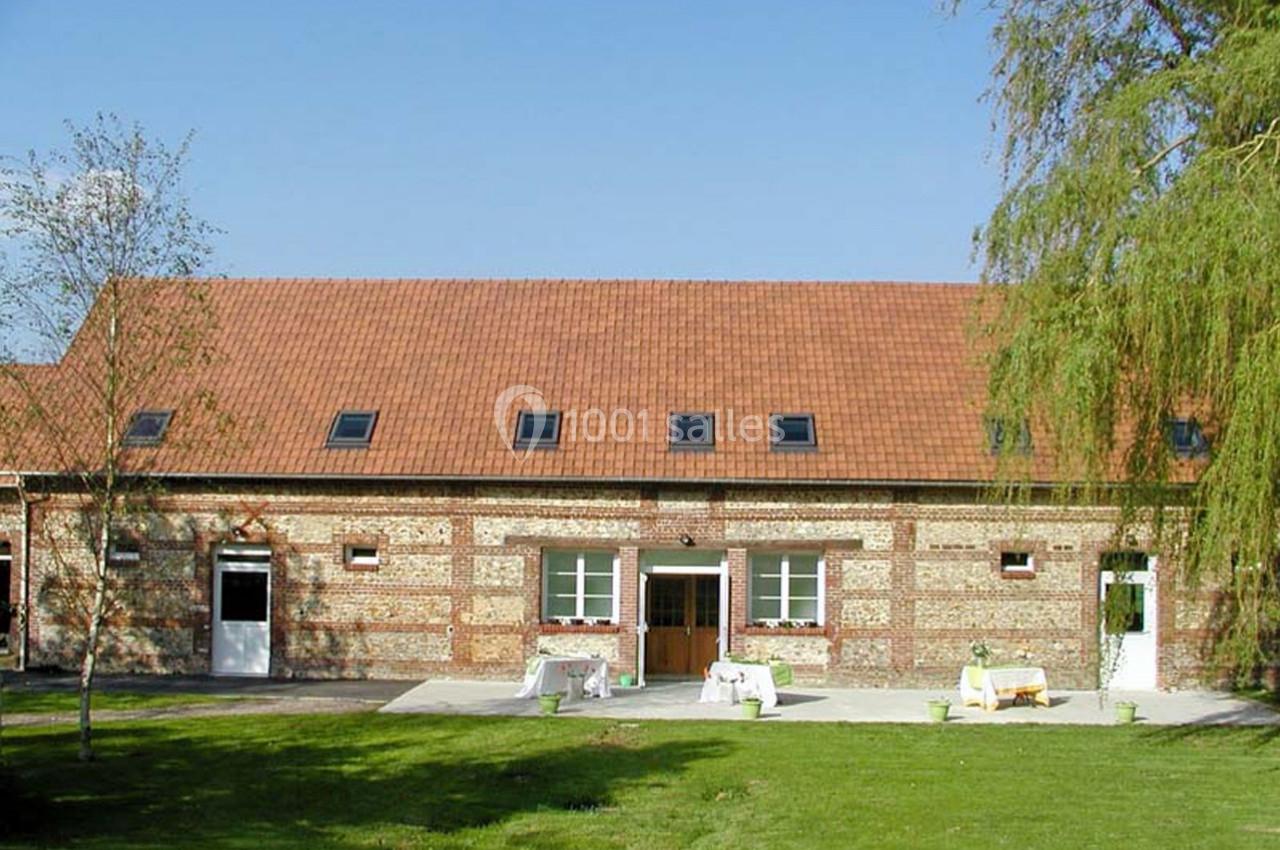 Bâtiment en briques avec toit en tuiles rouges, entouré d'une pelouse et d'arbres sous un ciel dégagé.