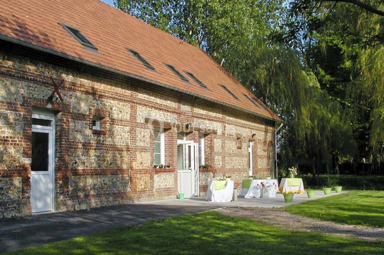 Façade en briques d'un bâtiment avec terrasse aménagée, tables dressées et jardin arboré en arrière-plan.