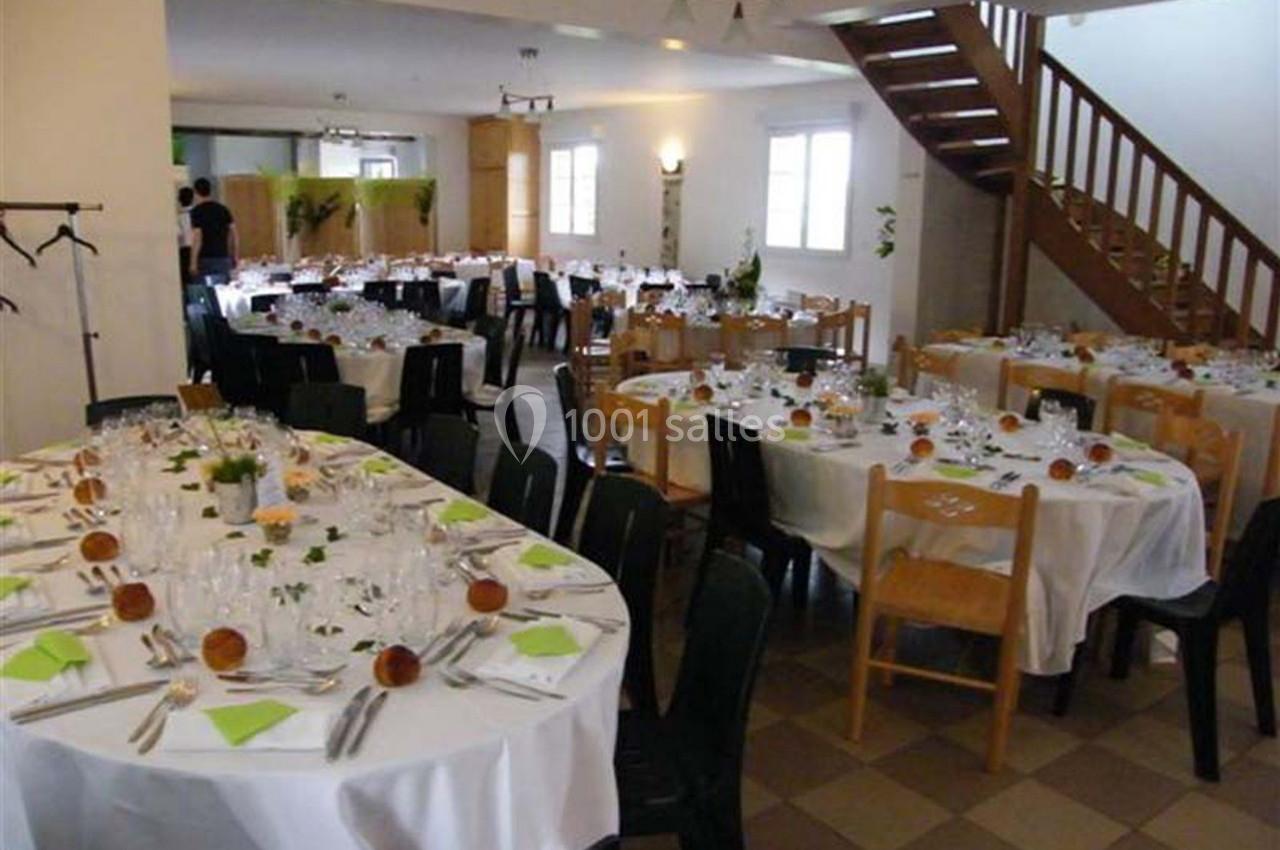 Salle de réception avec tables dressées, nappes blanches, serviettes vertes et chaises en bois et plastique.