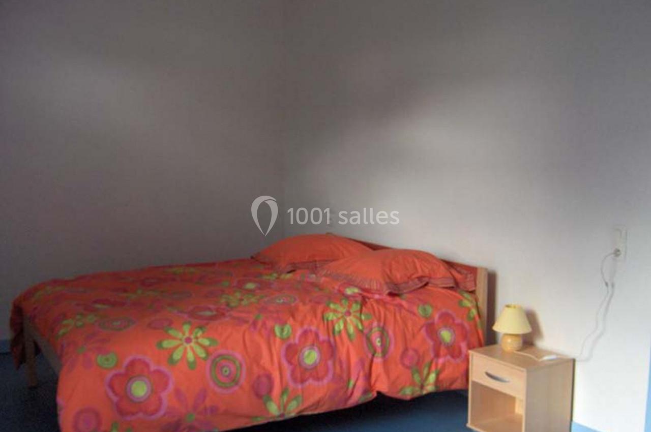 Lit double avec une housse de couette orange à motifs floraux, table de chevet en bois avec lampe dans une chambre sobre.