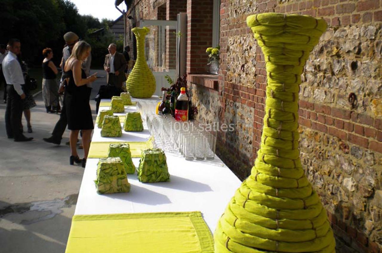 Table extérieure dressée avec des décorations vertes, des verres et des boissons, devant un bâtiment en briques.
