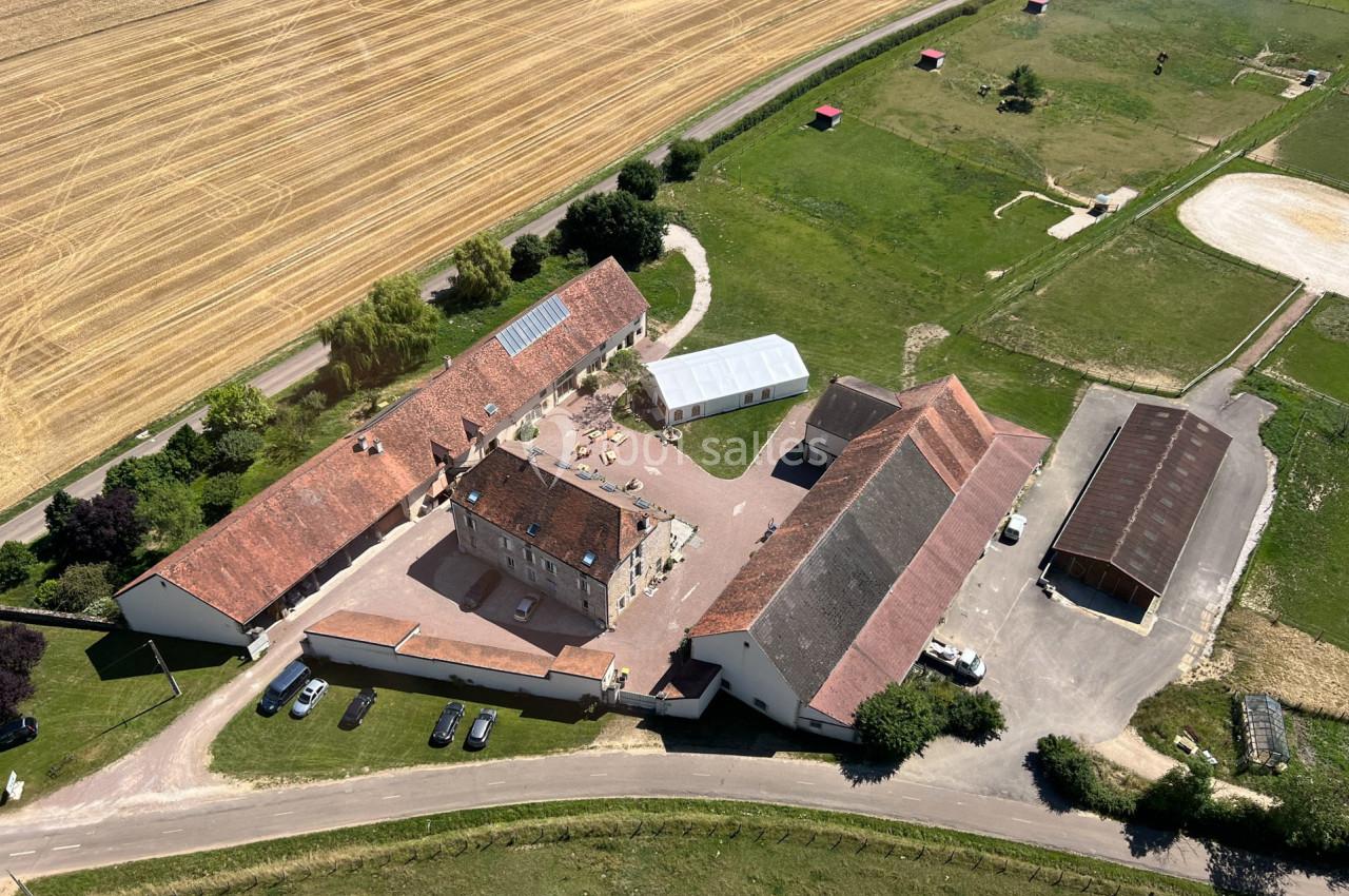 Vue aérienne d'un domaine rural avec bâtiments en pierre, cours centrale et champs environnants.