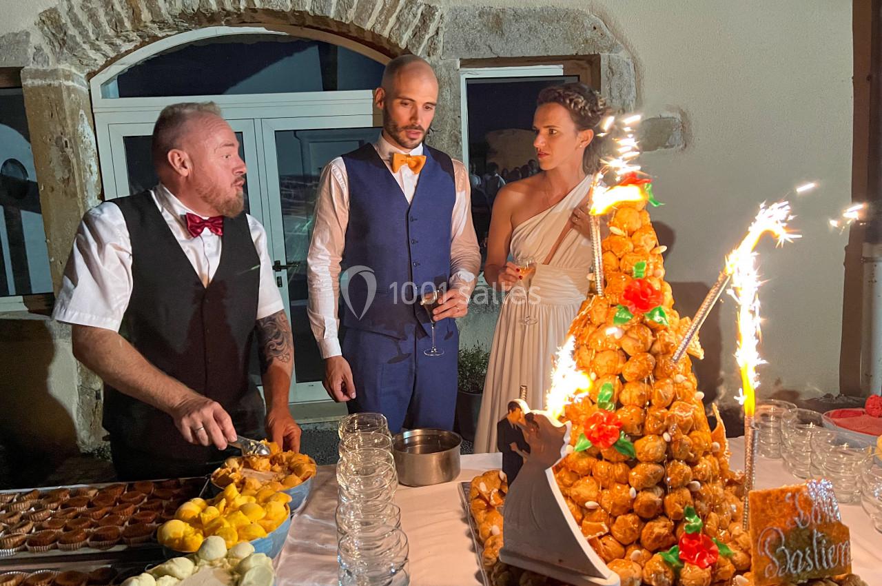 Un serveur présente un buffet de desserts avec une pièce montée éclairée par des étincelles, entouré de convives.