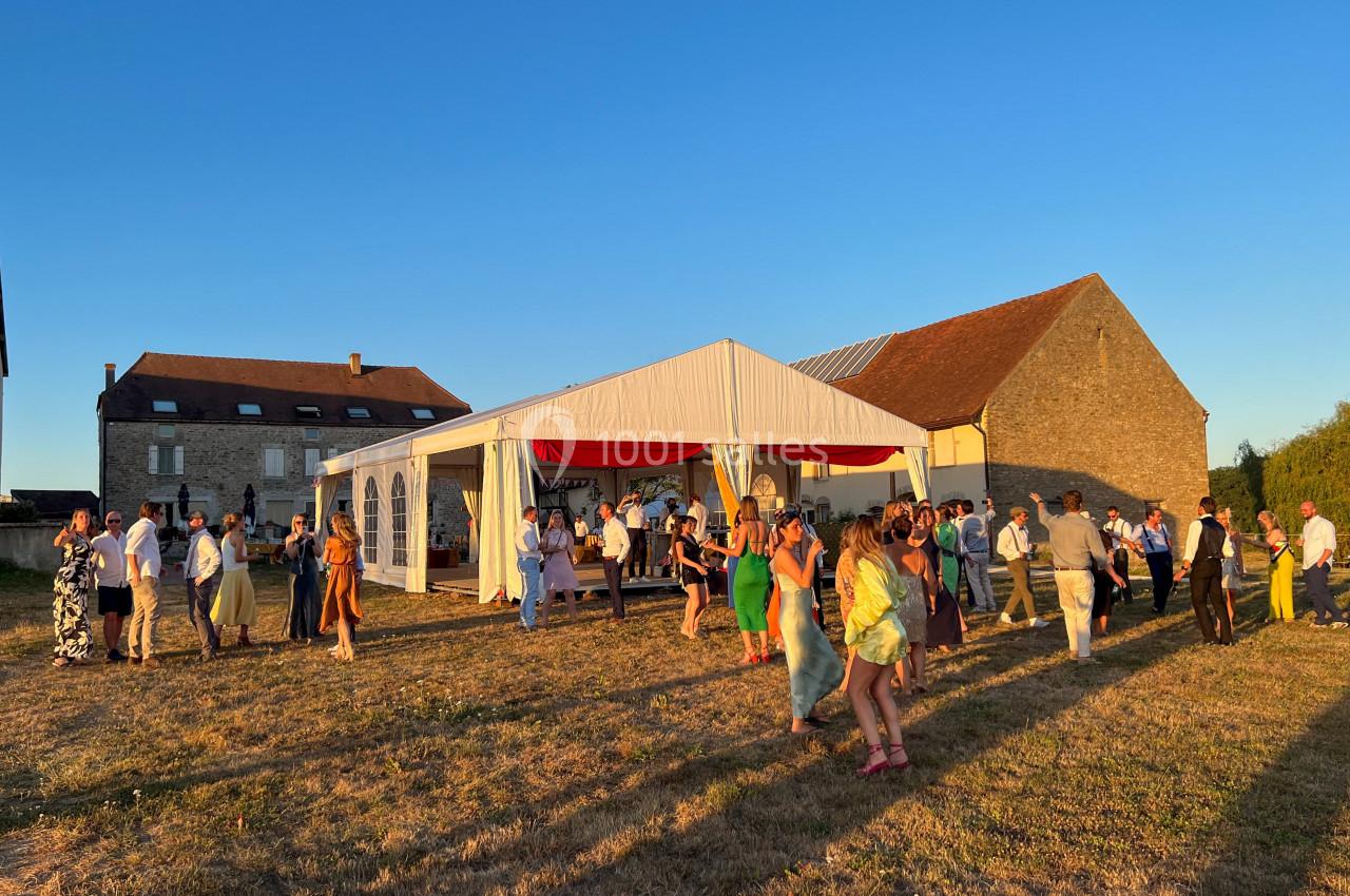 Groupe de personnes dansant et discutant devant une tente blanche lors d'une réception en plein air au coucher du soleil.