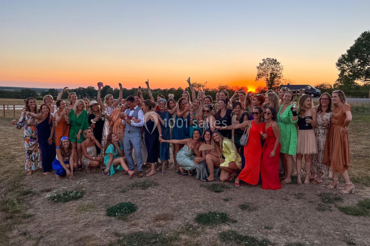 Un grand groupe de personnes posant joyeusement en plein air au coucher du soleil, sur un terrain herbeux.