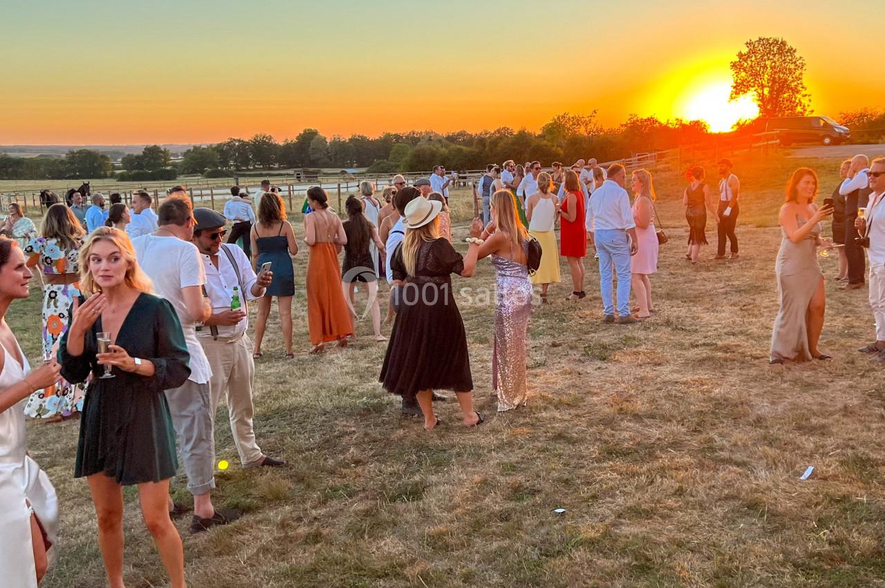 Groupe de personnes discutant en plein air lors d'un événement au coucher du soleil, dans un cadre champêtre.