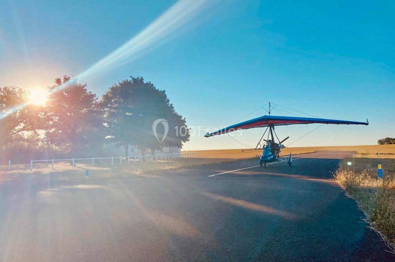 Un ULM à ailes rouges stationné sur une route ensoleillée près d'un champ et d'arbres.